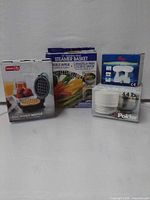 Front view of four boxed kitchen items: Dash waffle maker, Progressive steamer basket, Polder kitchen scale, additional digital scale