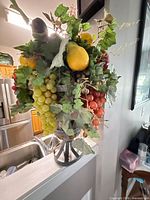 Front view showing assorted artificial fruits, leaves and metal urn base