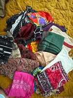 Mixed pile of assorted scarves and wraps spread on bed showing variety of colours and patterns