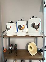 Three ceramic rooster canisters with lids, two small rooster figurines beneath, small oval bowl