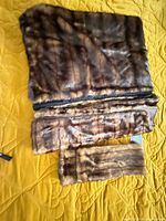 Three faux fur pieces: folded throw, scarf and muff displayed on yellow quilt