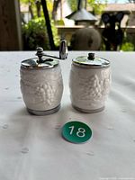 Front view of salt shaker and pepper mill showing milk glass bodies with grape motif and chrome tops