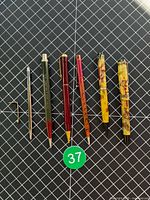 All six writing instruments laid out left to right on grid background