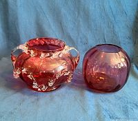 Both cranberry glass pieces side by side on blue backdrop