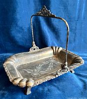 Angled view showing swing handle, floral engraving, ornate border and feet