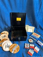 Overview of all items: metal box, coasters, thermometer card, advertising card, matchbooks