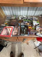 Overall view of mixed Xbox 360 cases, PS2 discs and board-game boxes on tabletop