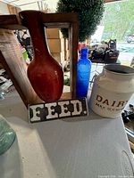 Group shot of red vase, blue bottle, metal milk can, wooden crate, FEED sign