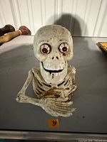 Front view of white cast iron skeleton bust coin bank with arms crossed and paint loss