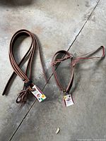Coiled brown leather split reins and matching noseband on concrete floor, tags visible