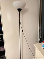 Full view of one torchiere lamp showing black pole, white bowl shade, inline switch on cord