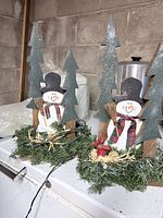 Two identical wood snowman centerpieces with lights and greenery bases