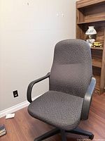 Front angled view of gray mid-back fabric office chair showing seat, back, armrests and part of swivel base