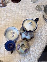 Top view of porcelain pitcher with lid, scalloped bowl, blue glass bowl in stand, covered trinket box