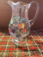 Front view of pitcher showing fruit and floral painting, footed base, gold rim.