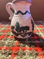 Front view of small ceramic pitcher showing bear, tree, zig-zag band