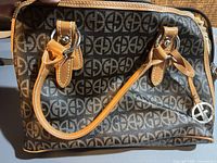 Front view of satchel showing monogram pattern, tan trim, dual handles, logo charm