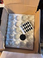 Foam tray holding multiple clear glass jars with black labels sheet