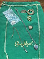 All jewelry pieces laid out on green Crown Royal fabric including necklaces, brooches, lockets and loose items