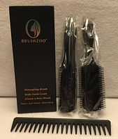 Box with Brushzoo branding alongside sealed detangling brush, 9-row brush and wide-tooth comb