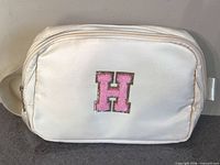 Front view of cream fanny pack showing pink H patch and main zipper