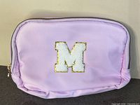 Front view showing light purple fanny pack, zipper, and white chenille letter M patch with gold glitter outline