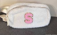 Front view of cream faux-shearling fanny pack showing pink S patch and zipper