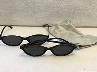 Two black oval sunglasses with dark lenses and grey pouch
