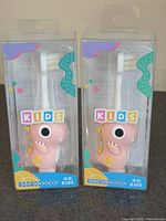 Front view of two boxed pink dinosaur kids toothbrushes
