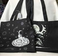 Both black space-themed tote bags front view, showing astronaut graphics