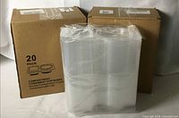 Front view showing two factory boxes labelled 20-pack and wrapped stack of clear double-compartment containers