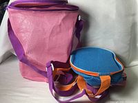 Pink and blue cylindrical mesh bags standing; shows size, material, straps