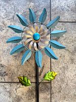 Close view of flower head showing turquoise petals, copper swirl, blue orb, and leaves