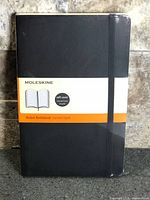 Front view of sealed black Moleskine notebook with original band