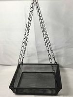 Square black wire mesh bird feeder with hanging chains.