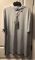 Front view of new Callaway grey-white striped golf polo on hanger showing overall style and condition