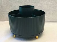 Side view showing ribbed exterior, gold-tone feet, dark green color