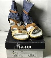 Front view of sandals on box showing tan suede straps, denim ankle cuffs, braided detail, and Geox branding