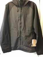 Front view of black McKinley softshell jacket showing full zip, hood and attached sales tag