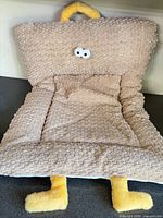 Front view of beige textured pet bed with eyes, handle, and yellow plush legs