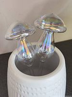 Two iridescent glass mushroom watering globes placed in a white pot