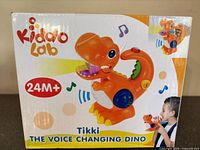 Front of retail box showing KiddoLab branding, Tikki Voice Changing Dino image, and 24M+ age label