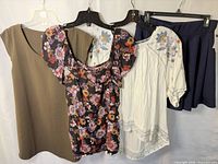 Group view of four garments on hangers: olive dress, floral dress, embroidered blouse, navy skirt