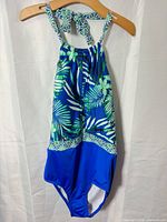 Front view of halter one-piece swimsuit showing palm leaf print, geometric trim, solid blue bottom