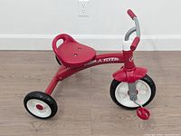 Right side view of red Radio Flyer tricycle showing frame, wheels, seat