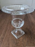 Front angled view of clear pressed glass footed vase showing flared ribbed rim and square pedestal