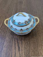 Front view of covered sugar bowl highlighting blue band, floral medallions and gold trim