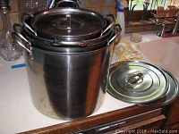 Four aluminum stock pots nested together with three lids, largest pot approximately 12x10 inches.