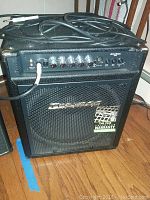 Front and top view of black Traynor Dynabass 100 guitar amplifier with control knobs, input jacks, and Fender cable attached.