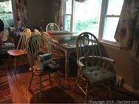 Six wooden kitchen chairs arranged around a table. Two armchairs have padded cushions. Others have curved spindle backs and wooden seats.